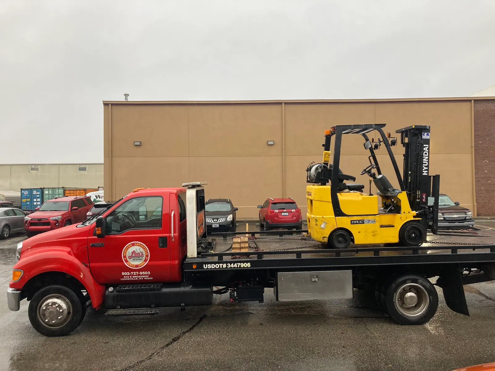 Red Leo's flatbed carrying a yellow forklift