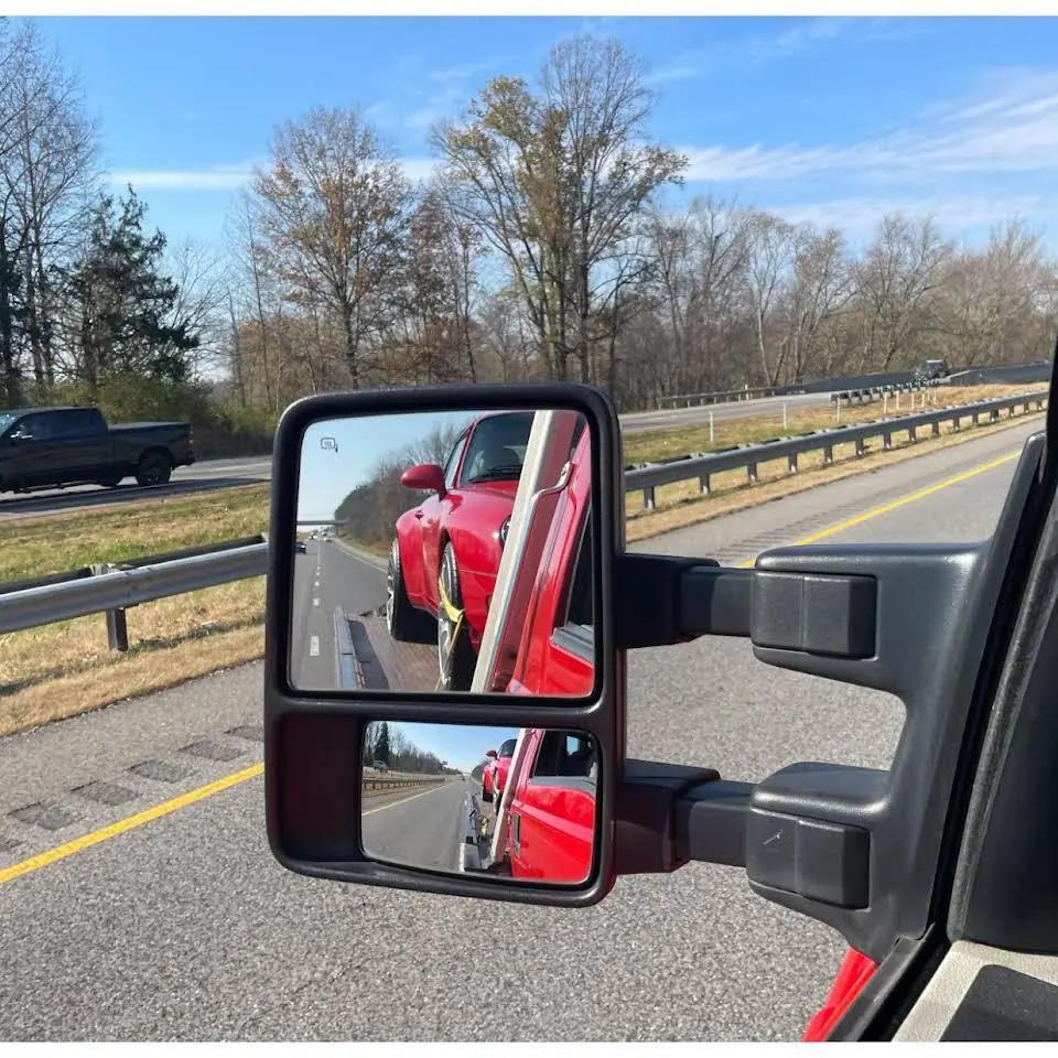 Truck side mirror reflecting a red car on the highway